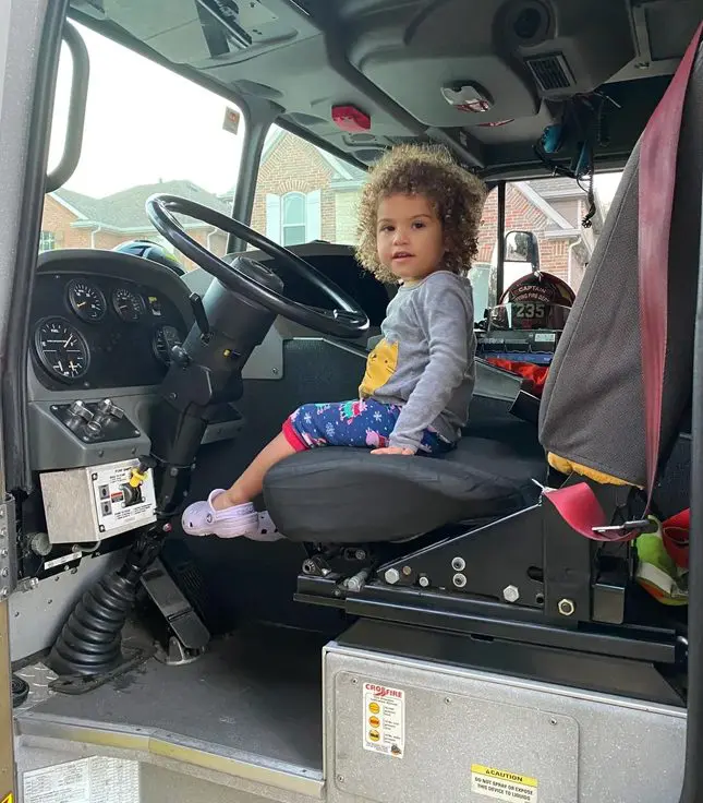 A little girl sitting in the driver 's seat of a fire truck.